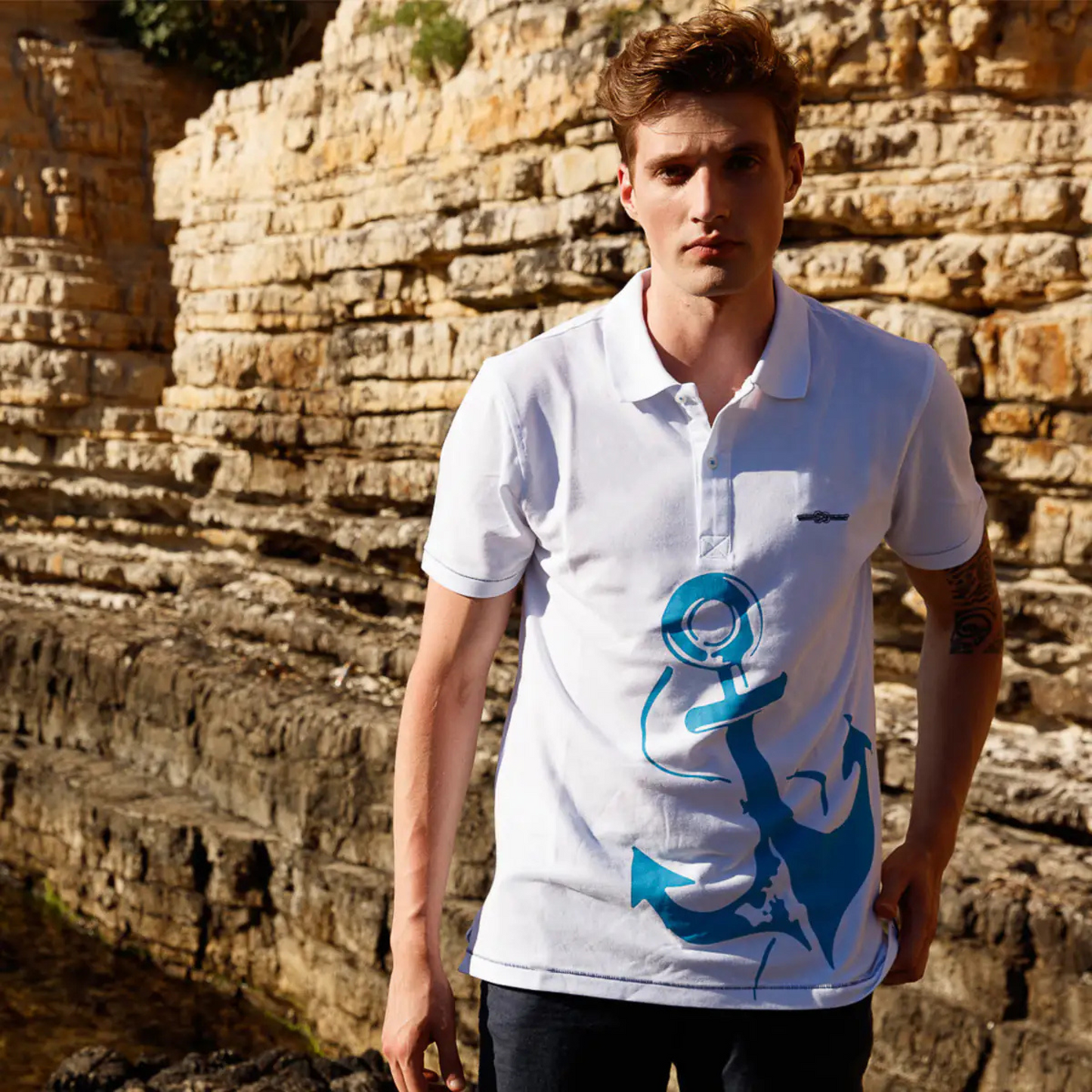 Men's Nautical Cotton Polo Shirt in white with a large aquamarine blue anchor graphic on the front, featuring a classic two-button collar and the embroidered Anemoss logo.