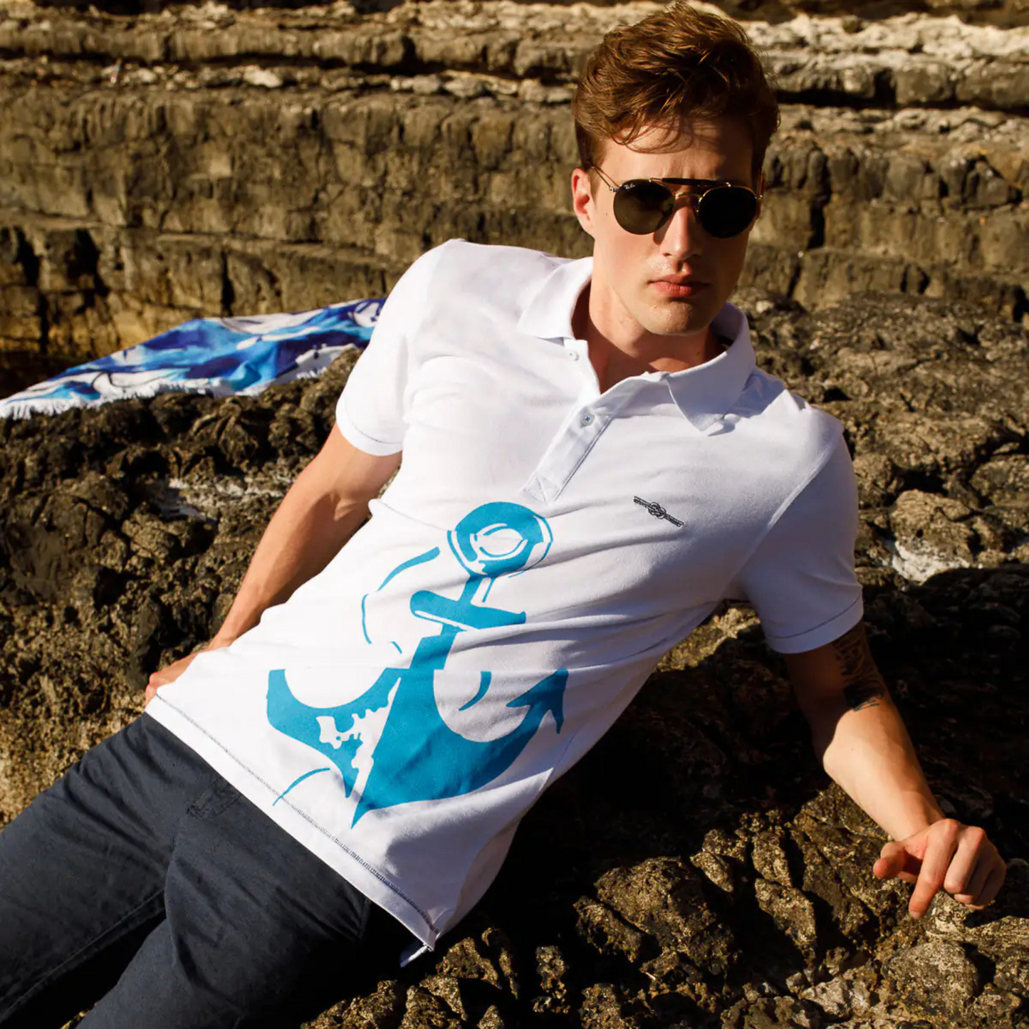 Men's Nautical Cotton Polo Shirt in white with a large aquamarine blue anchor graphic on the front, featuring a classic two-button collar and the embroidered Anemoss logo.