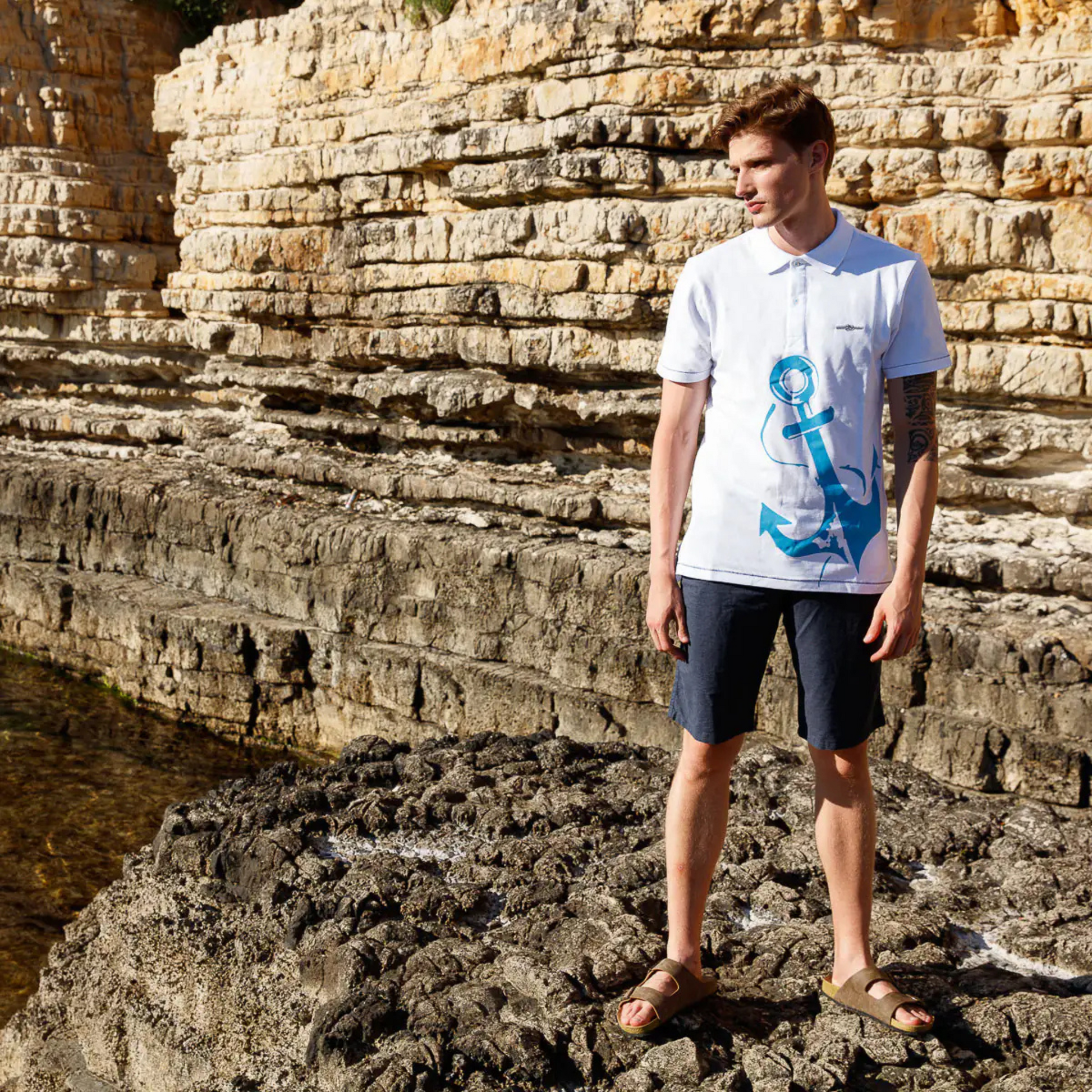 Men's Nautical Cotton Polo Shirt in white with a large aquamarine blue anchor graphic on the front, featuring a classic two-button collar and the embroidered Anemoss logo.